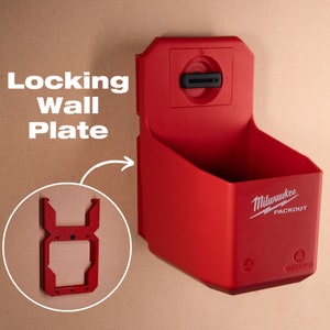 Può includere: Piastra da parete rossa in plastica con un meccanismo di bloccaggio e il testo "Milwaukee PACKOUT" sul davanti. La piastra è progettata per contenere utensili e altri oggetti.