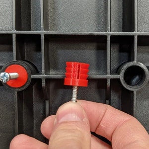 Op de afbeelding: Een rode plastic schroefanker met een zilveren schroef. Het anker heeft een geribbeld ontwerp en wordt gebruikt om voorwerpen aan een muur te bevestigen.