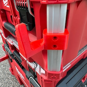 May include: A red and silver tool box with a red plastic handle. The handle is attached to a silver metal pole. The tool box has a black latch and a black handle.