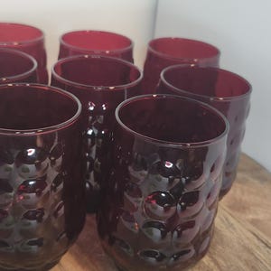 May include: Set of ten red glass tumblers with a textured, bubbled design. The glasses are arranged in a circle on a wooden surface.
