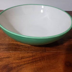 May include: A large, white bowl with a green rim. The bowl is sitting on a wooden surface.