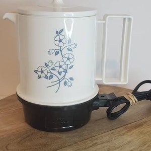 May include: White electric coffee pot with a blue floral design and a black base. The pot has a handle and a lid.