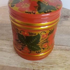 May include: A red wooden jar with a lid, decorated with gold and green floral patterns. The jar is hand-painted with traditional Russian folk art.