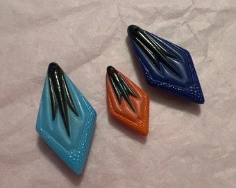 May include: Three diamond-shaped pendants with black and white designs. The pendants are blue, orange, and red.