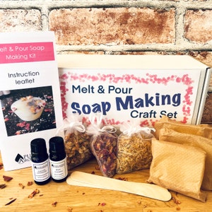 May include: A white box with the text "Melt & Pour Soap Making Craft Set" on the front. The box contains a variety of ingredients for making soap, including dried flowers, essential oils, and a wooden stirring stick.