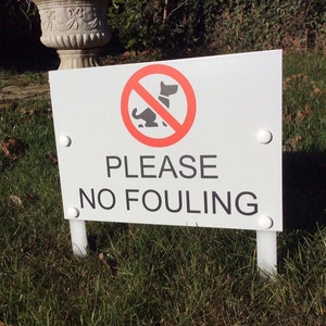 Op de afbeelding: Een wit bord met een rode cirkel en een zwart silhouet van een hond met een rode streep erdoorheen. Het bord staat er "PLEASE NO FOULING" op.