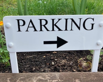 May include: White sign with black text and an arrow pointing to the right. The sign reads "PARKING".