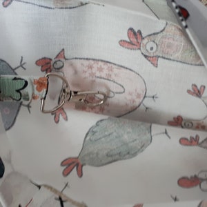 May include: White fabric with a repeating pattern of cartoon chickens. The fabric has a silver metal clip attached to it.
