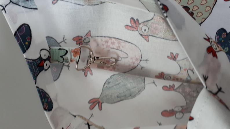 May include: White fabric with a repeating pattern of cartoon chickens. The fabric has a silver metal clip attached to it.