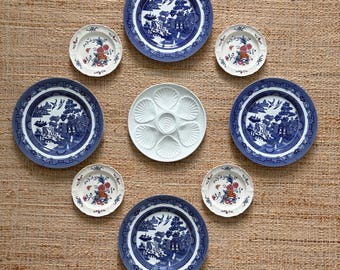 May include: A collection of decorative plates arranged in a circular pattern. The plates feature blue and white Chinoiserie designs and floral patterns. A white oyster plate is in the center. The plates are set on a textured, neutral-toned surface.