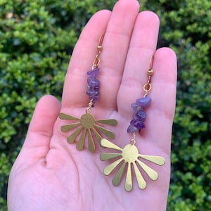 May include: Gold earrings with a sunburst design and amethyst gemstone accents.