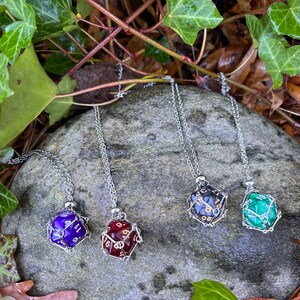 May include: Four silver necklaces with dice pendants. The dice are in a wire cage and are red, purple, black, and green.