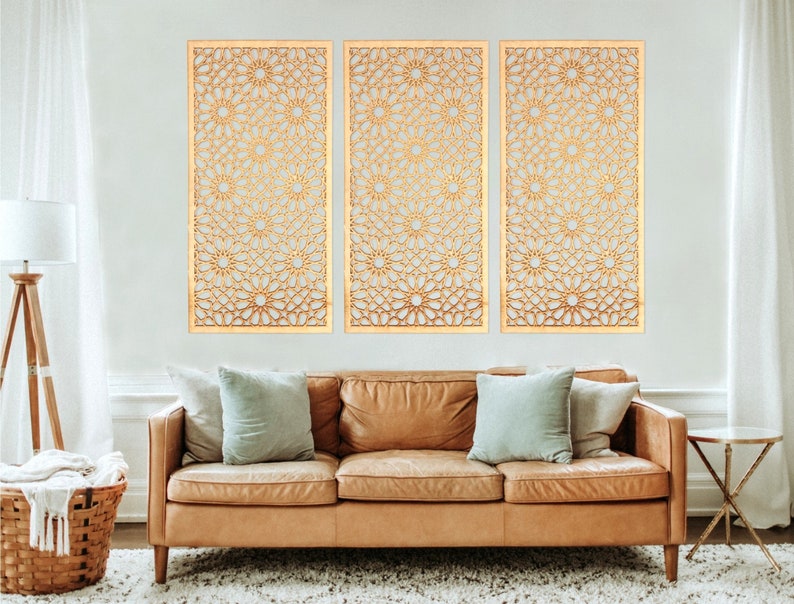 May include: Three gold-coloured metal wall decor panels with a geometric pattern. The panels are hanging on a white wall above a brown leather sofa.