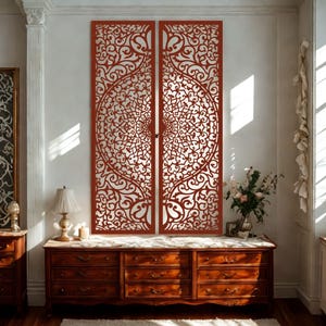 Può includere: Due pannelli decorativi da parete rossi con intricati disegni traforati a spirale. I pannelli sono esposti contro un muro bianco, con una cassettiera in legno e altri oggetti decorativi in primo piano. I pannelli sono un punto focale suggestivo.