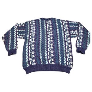 May include: A vintage sweater with a patterned design in shades of blue, purple, and white. The sweater features a ribbed hem and cuffs, with a crew neck. The sleeves are long and the overall style is a relaxed fit.