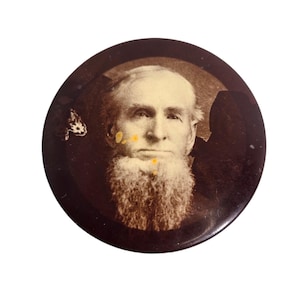May include: A vintage circular button featuring a sepia-toned portrait of an older man with a long white beard. The button has a dark brown border and shows signs of age.