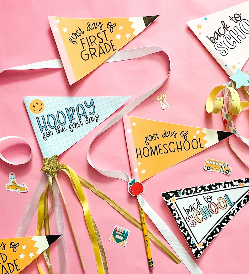 May include: Five colorful pennant flags with different back to school messages. The flags are decorated with stars, a pencil, and a school bus. The flags are on a pink background with ribbons and other school-themed decorations.