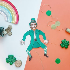 May include: A green leprechaun paper doll with a green hat, red hair, and a white beard. The doll is holding a pot of gold and is surrounded by shamrocks and coins.