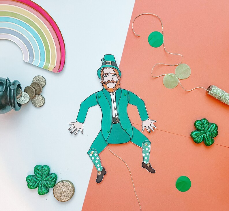 May include: A green leprechaun paper doll with a green hat, red hair, and a white beard. The doll is holding a pot of gold and is surrounded by shamrocks and coins.