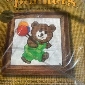 May include: A needlepoint kit featuring a brown bear holding three balloons. The kit includes 100% cotton canvas, 100% wool yarn, and instructions. The kit is designed by Lynn Davis and is called "Barney".