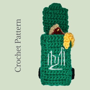 Op de afbeelding: Een handgemaakt groen gehaakt item met een rechthoekig lichaam en een bovenstuk. Het heeft een wit geborduurd ontwerp en een kleine, kleurrijke versiering. De tekst "Crochet Pattern" is zichtbaar.