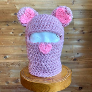 May include: Pink crocheted balaclava with heart-shaped ears and a heart detail on the front.