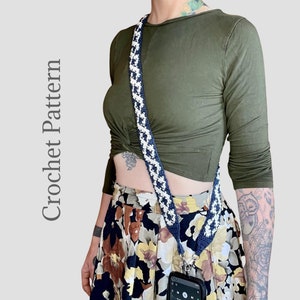 May include: A crocheted phone strap with a black and white checkered pattern. The strap is worn over a green shirt and a floral skirt.