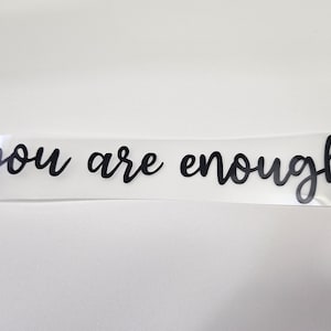 May include: A clear vinyl sticker with the text "you are enough" in black cursive lettering.