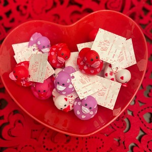 May include: A red heart-shaped bowl filled with small rubber duck toys. The ducks are decorated with pink and white polka dots and have a message on the tag that says "You Quack Me Up".