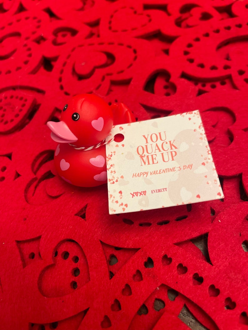 May include: Red rubber duck with white polka dots and a pink beak. The duck is sitting on a red felt background with a white card that says "You Quack Me Up Happy Valentine's Day XOXO Everett".