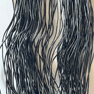 May include: A close-up of a bundle of black elastic cord. The cord is thin and flexible, and it is arranged in a random pattern.