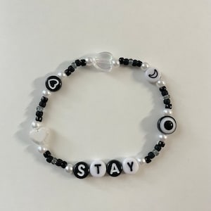 May include: A black and white beaded bracelet with the word "STAY" spelled out in white beads. The bracelet also features a heart, a crescent moon, and an evil eye charm.