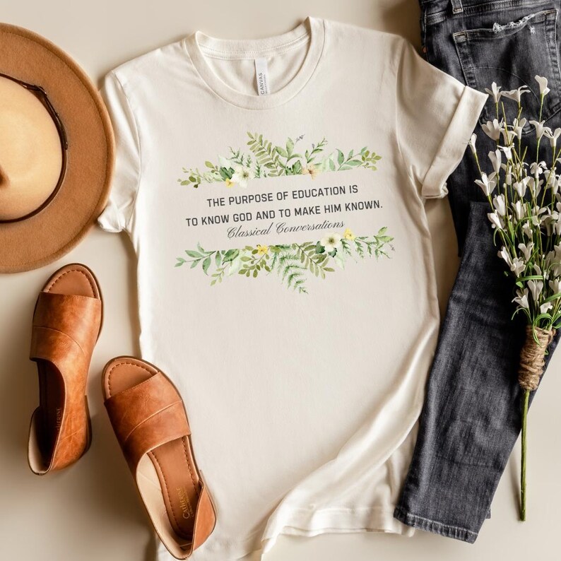 May include: A white t-shirt with a floral design and the text "THE PURPOSE OF EDUCATION IS TO KNOW GOD AND TO MAKE HIM KNOWN. Classical Conversations".
