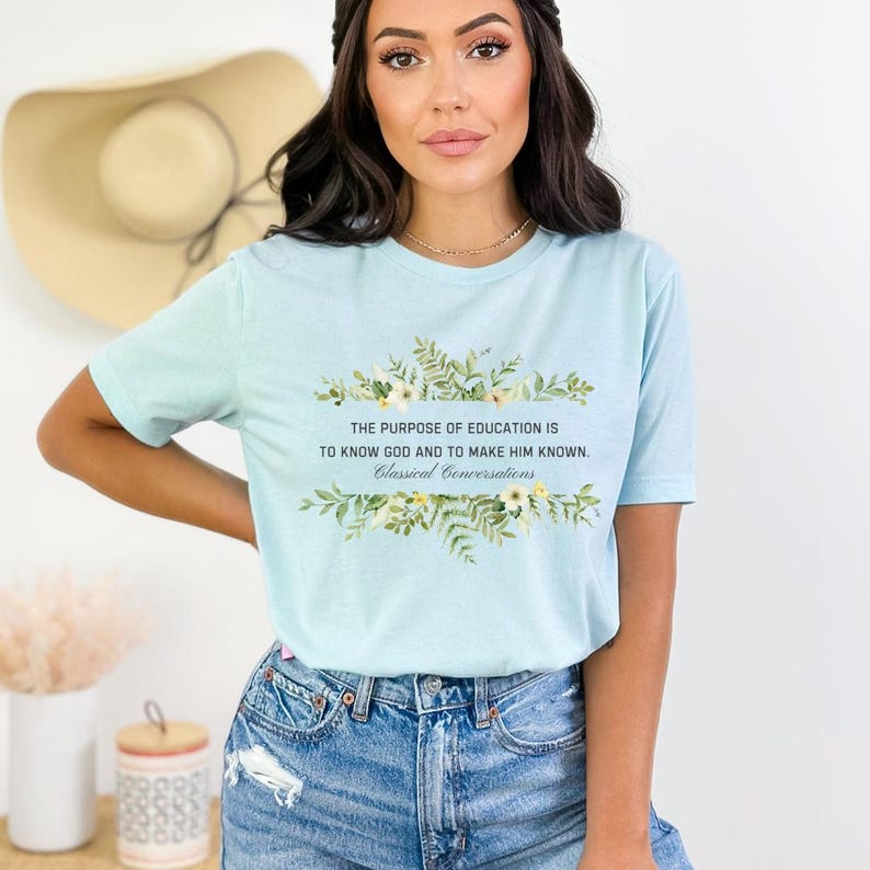 May include: Light blue t-shirt with a floral design and the text "THE PURPOSE OF EDUCATION IS TO KNOW GOD AND TO MAKE HIM KNOWN. Classical Conversations".