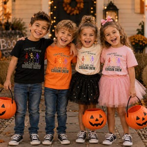 May include: Four children wearing matching t-shirts with the text 'YOU CAN'T SCARE US WE ARE THE COUSIN CREW' and colorful skeleton graphics. The shirts are black, orange, cream, and pink. Two children wear blue jeans, and two wear tulle skirts.