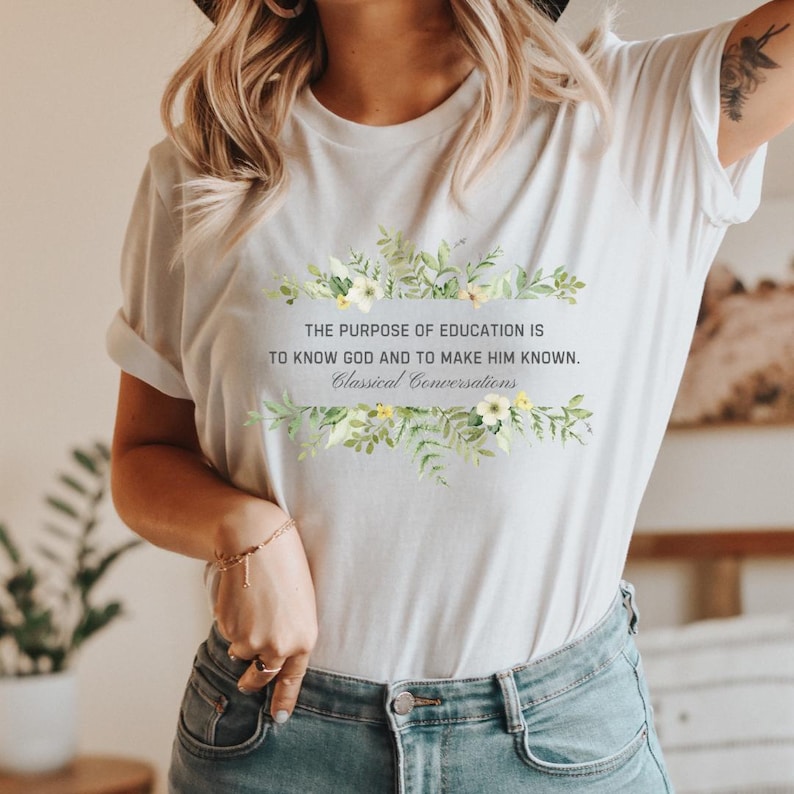 May include: White t-shirt with a floral design and the text "THE PURPOSE OF EDUCATION IS TO KNOW GOD AND TO MAKE HIM KNOWN. Classical Conversations".