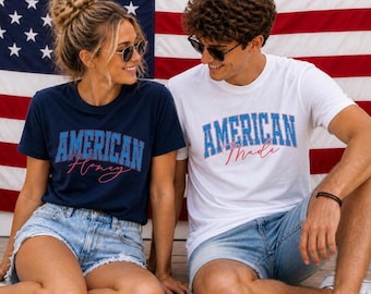 May include: Two people wearing t-shirts with patriotic text in front of an American flag. One shirt is navy blue with "AMERICAN Honey" in blue and pink. The other is white with "AMERICAN Made" in blue and red.