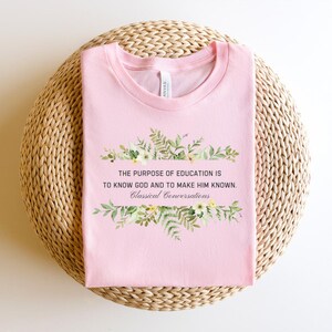 May include: Pink t-shirt with a floral design and the text "THE PURPOSE OF EDUCATION IS TO KNOW GOD AND TO MAKE HIM KNOWN. Classical Conversations".