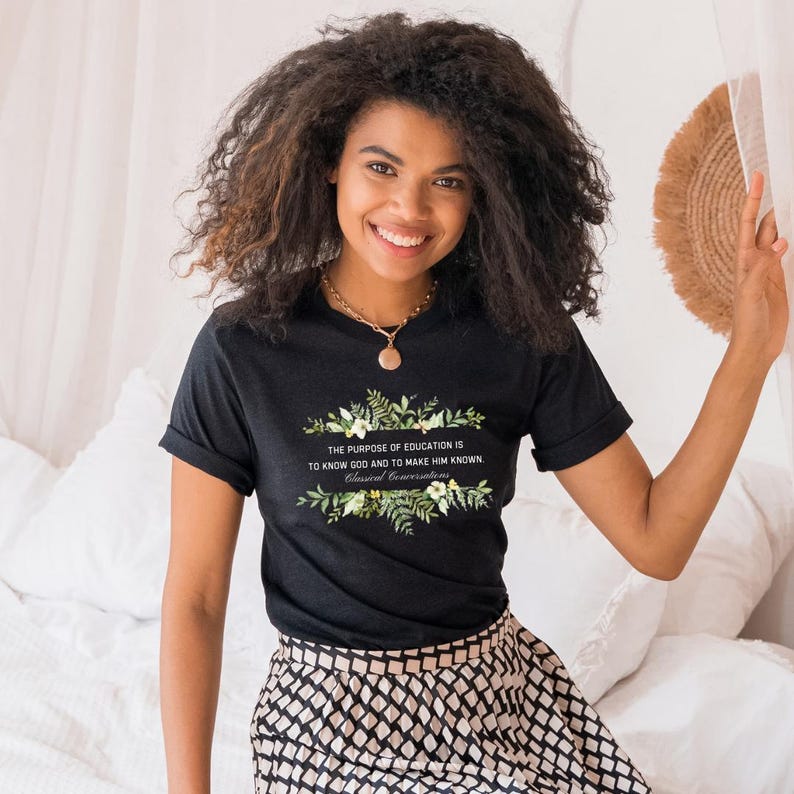 May include: Black t-shirt with a floral design and the text "THE PURPOSE OF EDUCATION IS TO KNOW GOD AND TO MAKE HIM KNOWN. Classical Conversations".