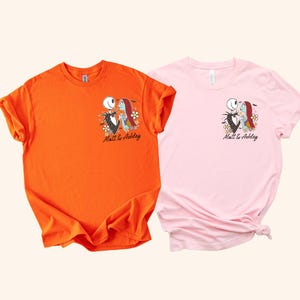 Puede incluir: Dos camisetas, una naranja y otra rosa, cada una con un gr&aacute;fico de Jack y Sally de The Nightmare Before Christmas. El dise&ntilde;o incluye el texto "Matt & Ashley" debajo de los personajes, con detalles florales.