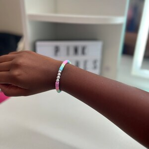 Puede incluir: Un brazalete de cuentas de colores con cuentas de color rosa pastel, azul, verde y blanco. El brazalete tiene cuentas espaciadoras plateadas.