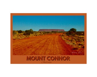 Op de afbeelding: Een rode zandweg leidt naar een grote, platte berg in de verte. De lucht is blauw en het landschap is droog en kaal. De tekst "MOUNT CONNOR Australia" staat onderaan de afbeelding.