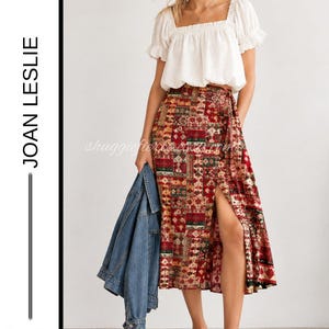 May include: A white square-neck blouse with short puff sleeves paired with a high-waisted midi skirt featuring a red, green, and gold patchwork pattern and a front slit. A blue denim jacket is held at the side. Text reads JOAN LESLIE SIZE 12P.