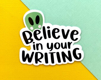 Può includere: Un adesivo bianco con la scritta "Believe in your WRITING" in grassetto, in nero. L'adesivo presenta una testa di alieno verde con occhi neri e uno sfondo bianco. L'adesivo è su uno sfondo giallo e azzurro.