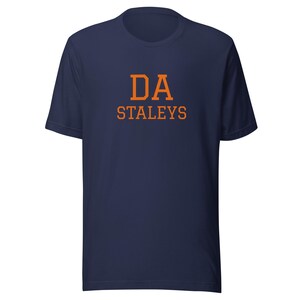 May include: A navy blue t-shirt with the text "DA STALEYS" printed in orange.