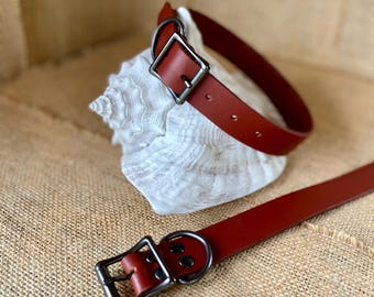May include: A red leather dog collar with a silver buckle and a matching leash. The collar and leash are lying on a burlap surface.