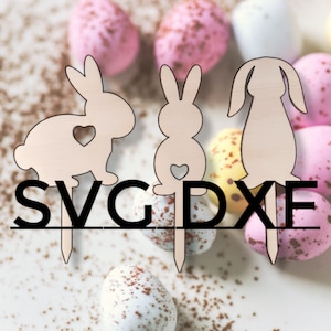 Könnte beinhalten: Drei hölzerne Hasenschnitte mit einem Herz auf der Brust. Die Hasen sind auf Stöcken und von Schokoladeneiern umgeben. Der Text "SVG DXF" ist unter den Hasen gedruckt.