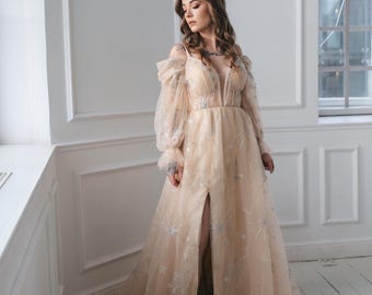 May include: A woman wearing a long, flowing, off-the-shoulder, light beige gown with a high slit and delicate floral embroidery. The gown has a fitted bodice and a full skirt.