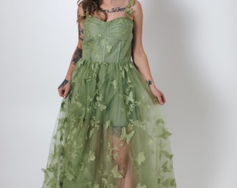 May include: A woman wearing a sage green tulle gown with butterfly embroidery. The gown has a fitted bodice and a flowing skirt. The woman is wearing nude heels.