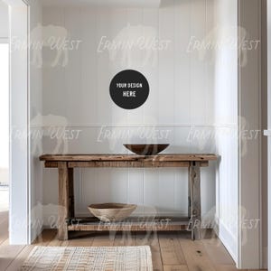 May include: A rustic wooden console table with a distressed finish, featuring a round wooden bowl and a woven basket on the lower shelf. The table is set against a white wall with a black circle that says "Your Design Here".
